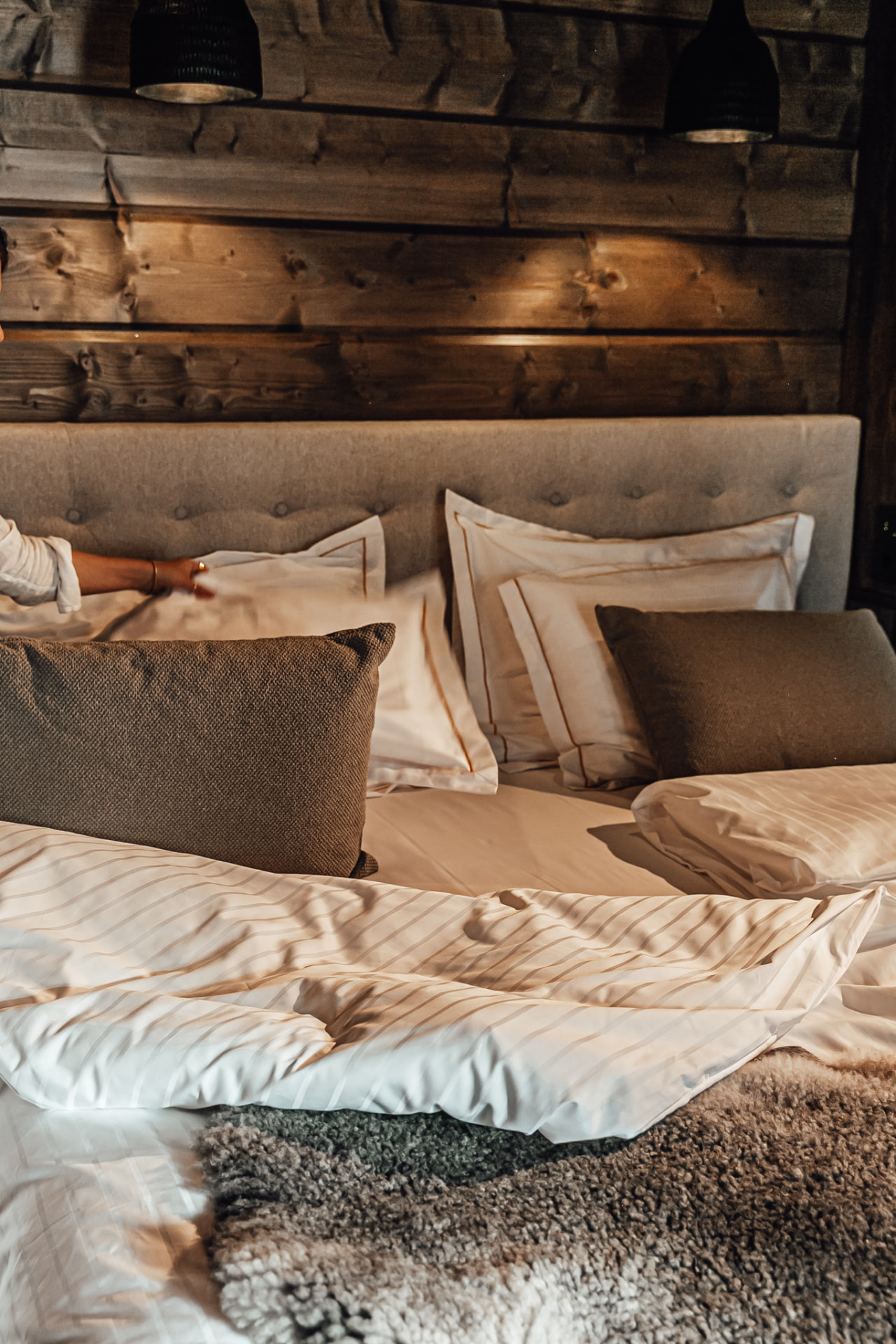 Pillows and white linen against a dark timber wall in a suite at Neituri Manor, Konnevesi