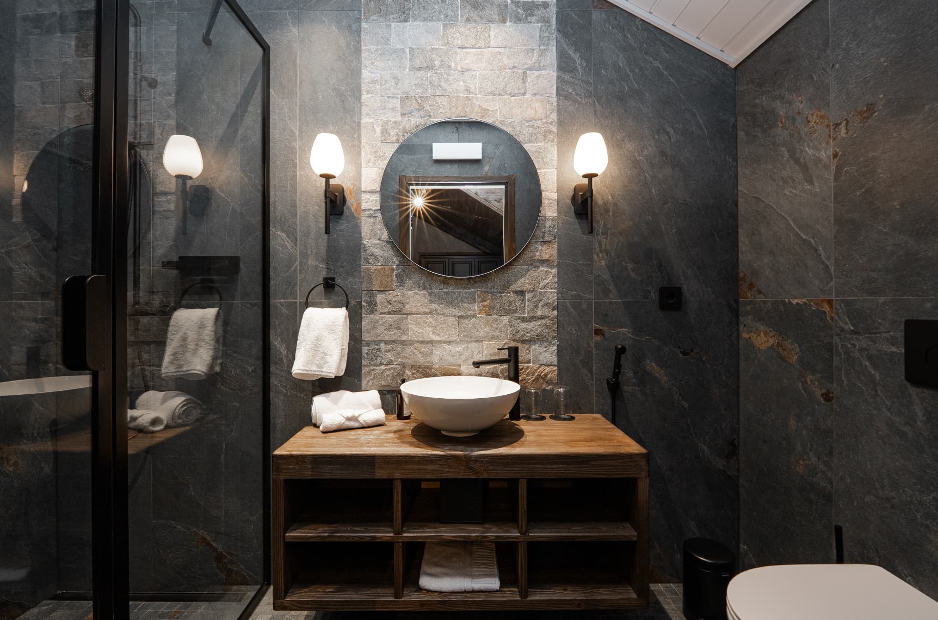 Guest bathroom with a round mirror and stone wall at Neituri Manor, Nordic luxury detail