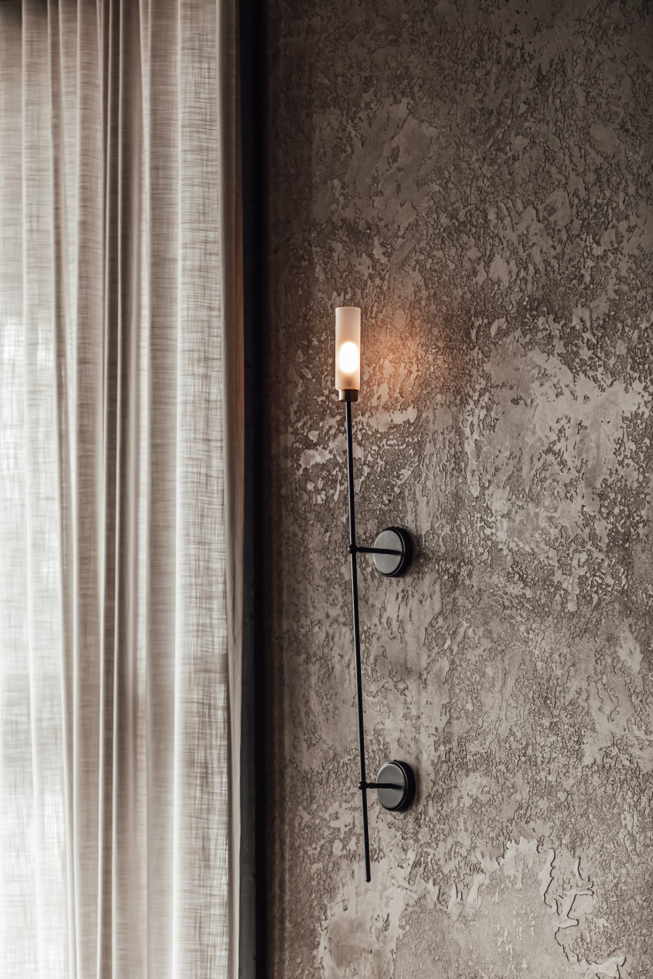 Slender sconce on a plaster wall beside the curtain, Scandinavian design detail at Neituri Manor